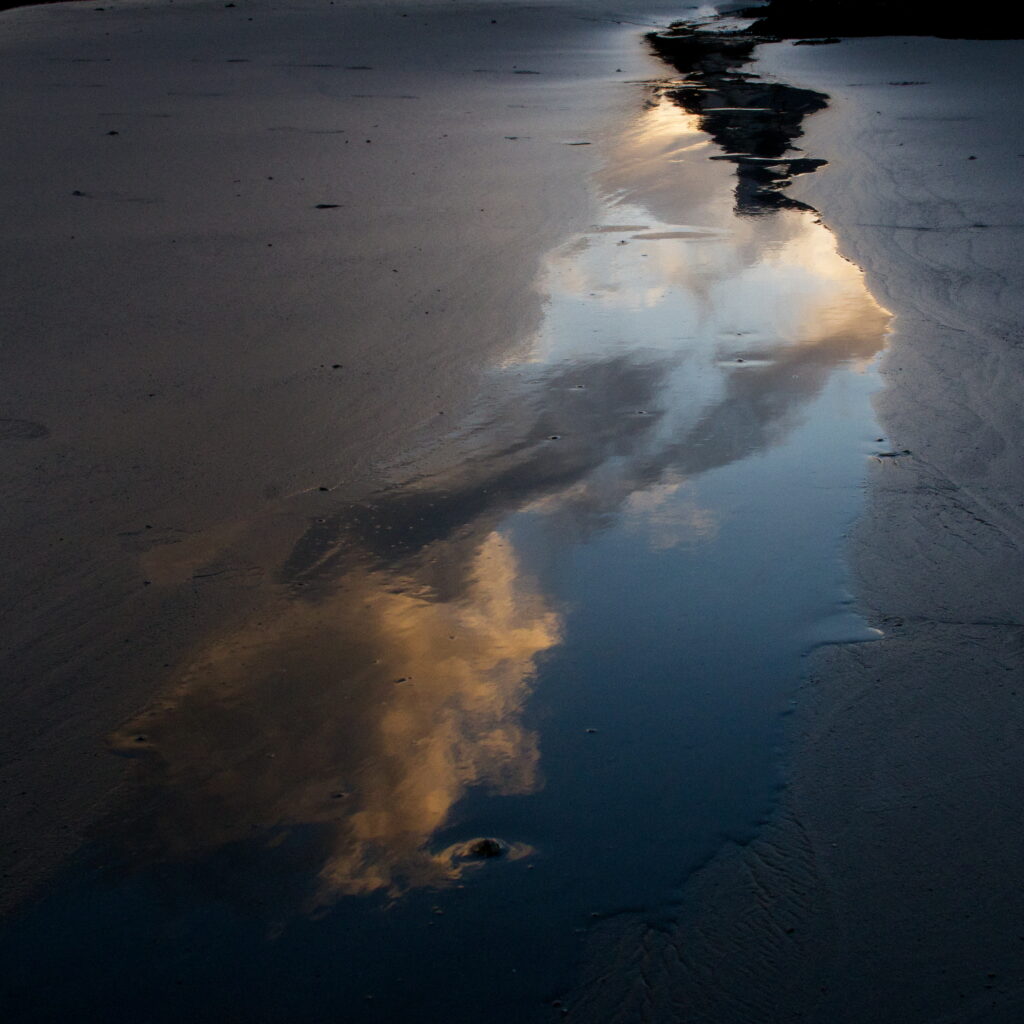 Reflets des nuages dans une grande flaque d’eau sur la plage.