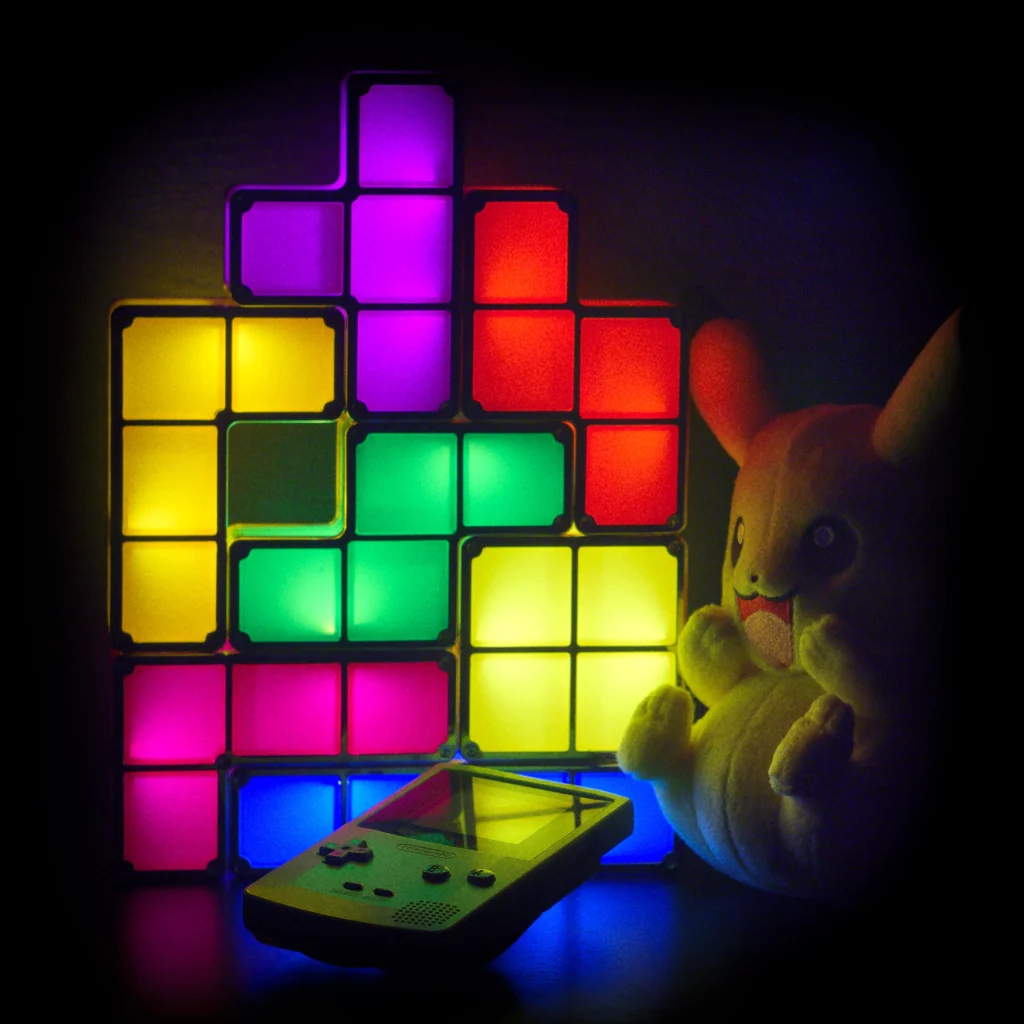 Photo d’une lampe tetris en fond, une gameboy color verte en bas et une peluche pikachu a droite.