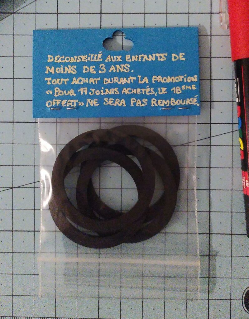 Petit sachet de joints d'étanchéité avec une étiquette bleue dessus : "déconseillé aux enfants de moins de 3 ans. Tout achat durant la promotion "pour 17 joints achetés le 18eme offert" ne sera pas remboursé."